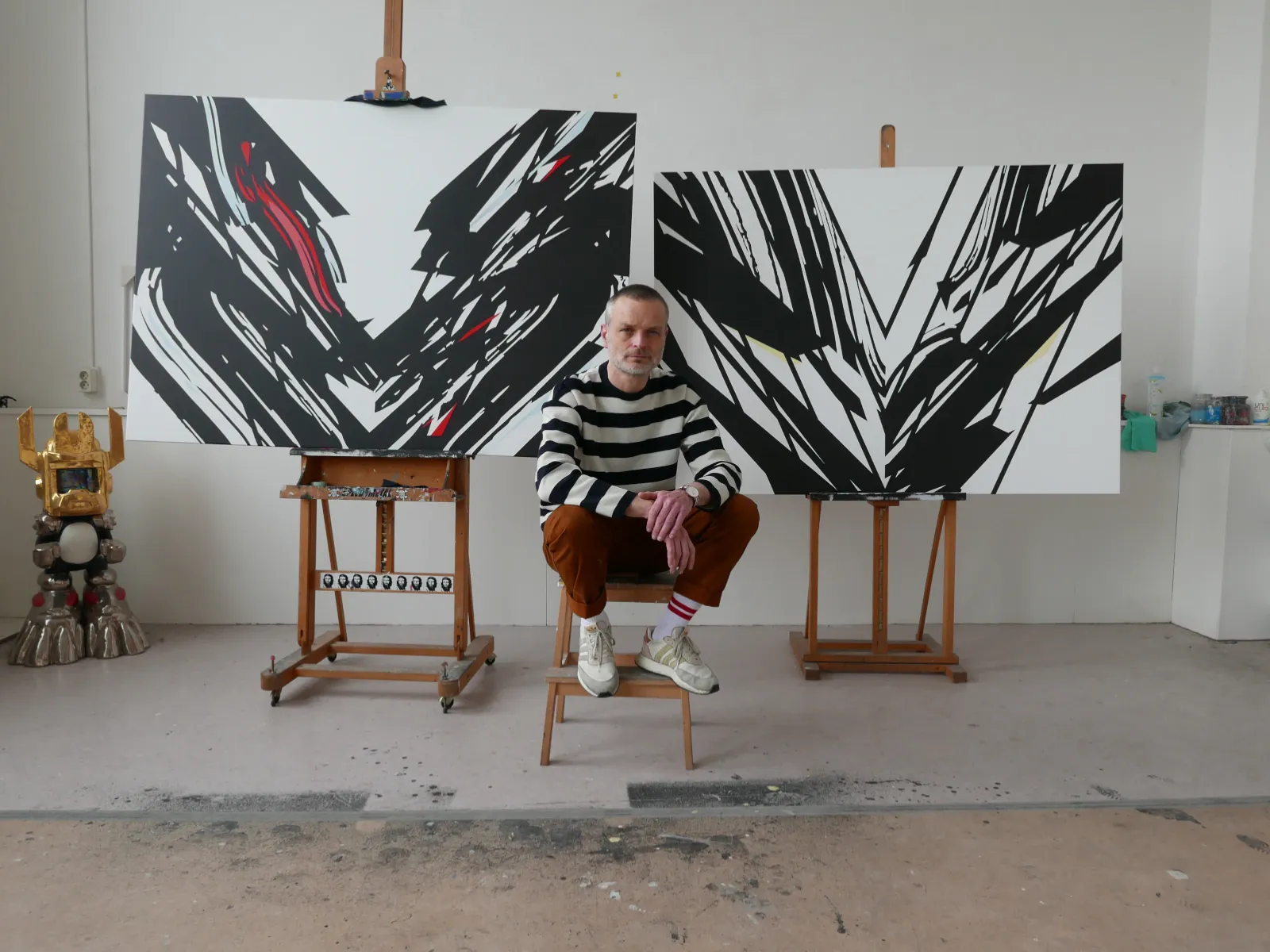Luuk Bode seated in his studio in front of his paintings